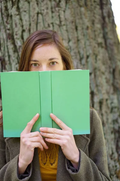 Young woman hiding behind a hardcover book — Stock Photo, Image