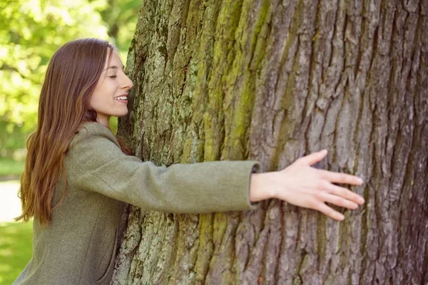 Mujer morena sonriente abrazando tronco de árbol — Foto de Stock