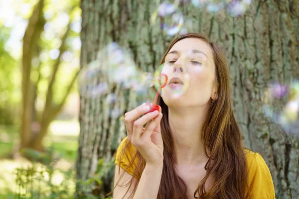 Feliz joven soplando burbujas en un parque — Foto de Stock