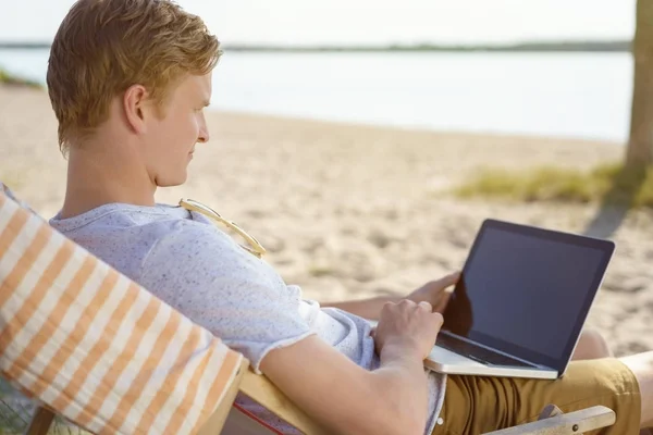 在海滩上工作笔记本电脑的年轻人 图库图片