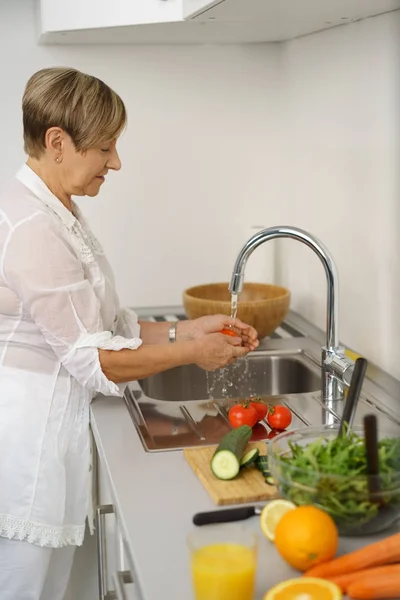 Seniorin wäscht Gemüse in Küchenspüle — Stockfoto