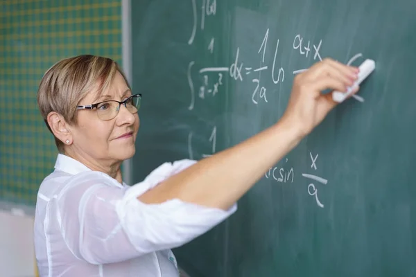 Senior female teacher writing on blackboard — Stock Photo, Image