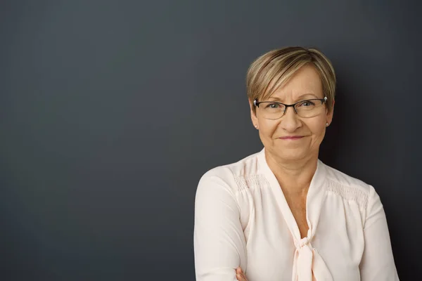 Femme âgée gaie appuyée contre un mur sombre — Photo