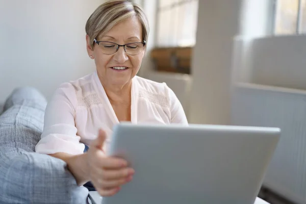 老年妇女在沙发上使用笔记本电脑 — 图库照片