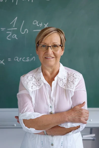 Female senior teacher standing against blackboard — Stock Photo, Image