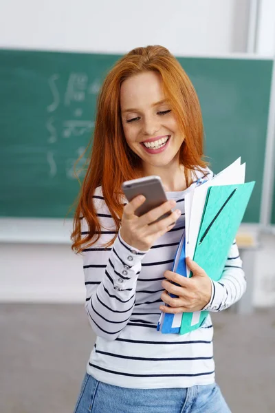 Jolie jeune étudiante rousse lisant un sms — Photo