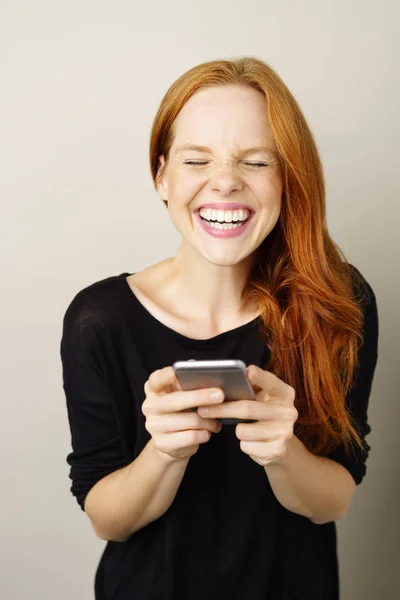 Młoda Ruda kobieta śmiejąc się z telefonu komórkowego — Zdjęcie stockowe