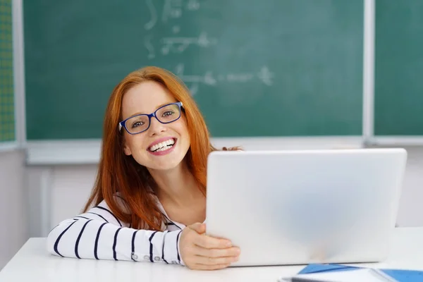 Jonge lachende vrouw zit aan bureau met laptop — Stockfoto