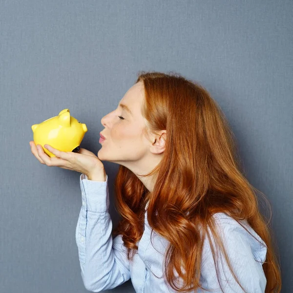 Young ginger woman kissing piggy bank — Stock Photo, Image