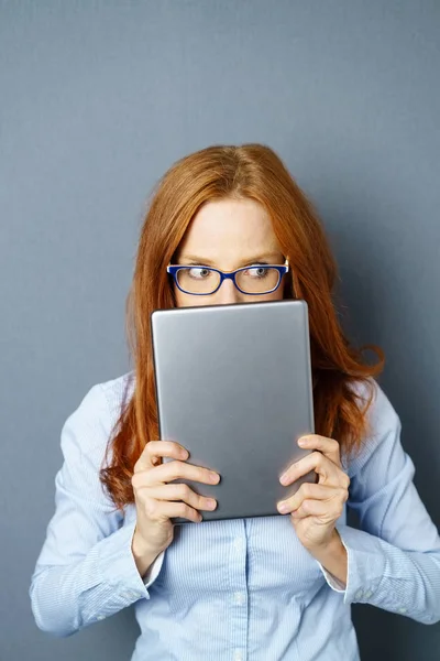 Mujer joven pelirroja cubriendo la cara con la tableta — Foto de Stock