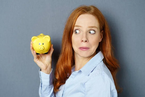 Young woman looking sceptically at her piggy bank — Stock Photo, Image