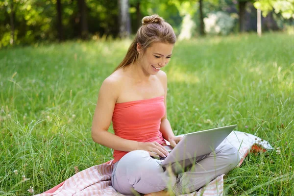 Ung kvinna sitter på gräs med bärbar dator — Stockfoto