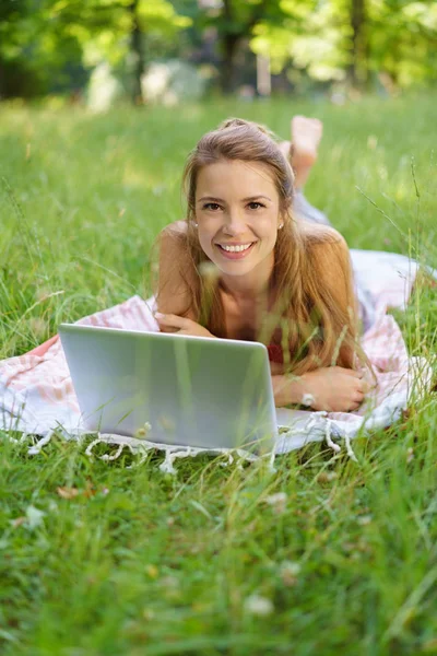 Çim üzerinde yalan sırasında dizüstü bilgisayar kullanan genç kadın — Stok fotoğraf