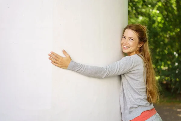 Joyeux jeune femme étreignant un pilier blanc — Photo