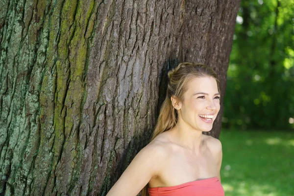 Unga leende kvinna som står vid träd — Stockfoto
