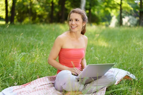 Giovane donna seduta sull'erba utilizzando il computer portatile — Foto Stock