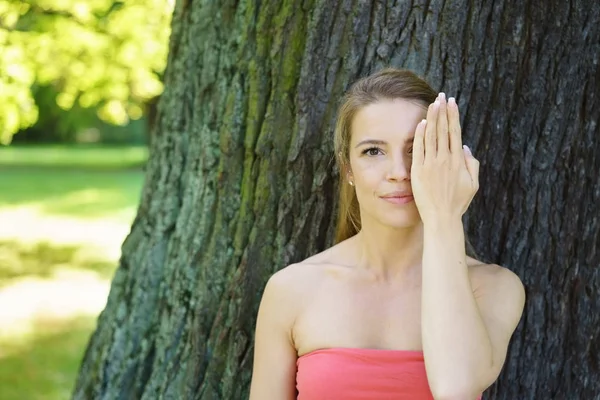 Mujer joven cubriendo su ojo contra el árbol — Foto de Stock