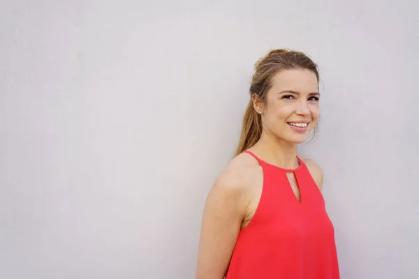 Giovane donna sorridente in piedi vicino al muro bianco — Foto Stock