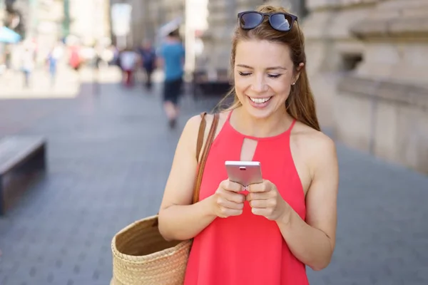 Uśmiechnięta dziewczyna ubrana w czerwoną sukienkę za pomocą telefonu komórkowego — Zdjęcie stockowe