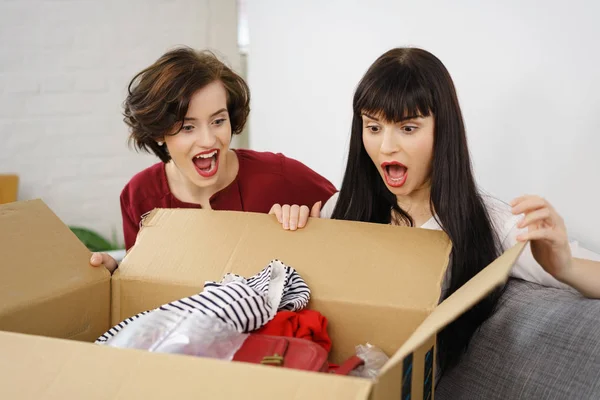 Zwei junge überraschte Frauen beim Auspacken von Kleidung — Stockfoto