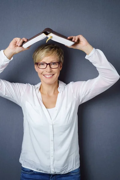 Mittlere erwachsene blonde Frau mit Buch über dem Kopf — Stockfoto