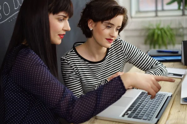 Dos mujeres atractivas con estilo que trabajan en un ordenador portátil — Foto de Stock