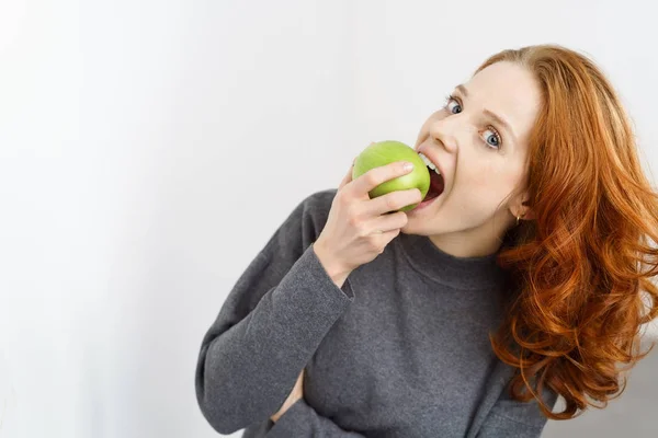 Гарненька молода жінка кусає зелене яблуко — стокове фото