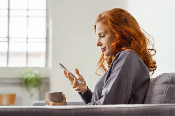 Junge Frau entspannt zu Hause mit ihrem Handy — Stockfoto