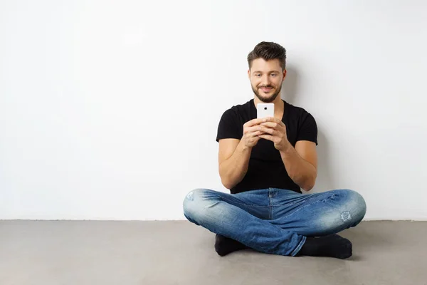 Młody człowiek siedzi na podłodze ze smartfonem — Zdjęcie stockowe