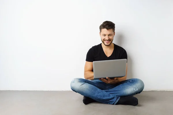 Ung man sitter av vit vägg med laptop — Stockfoto