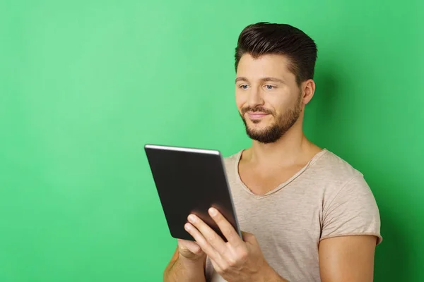 Joven sosteniendo la tableta contra fondo verde — Foto de Stock