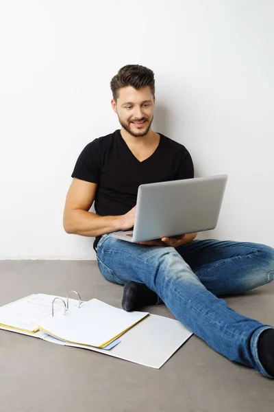 Молодий чоловік сидить біля стіни з ноутбуком і зв'язувачем — стокове фото