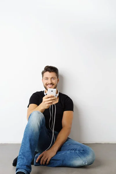 Giovane uomo seduto sul pavimento durante l'utilizzo di smartphone — Foto Stock