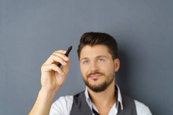 Young bearded man writing in air with pen — Stock Photo, Image