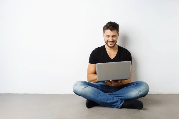 노트북으로 흰 벽에 앉아 젊은 남자 — 스톡 사진
