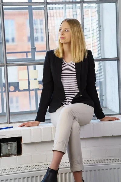 Promyšlené blondýnka sedí proti okno — Stock fotografie