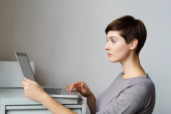 Dizüstü bilgisayar ile dosya dolabı tarafından duran genç kadın — Stok fotoğraf