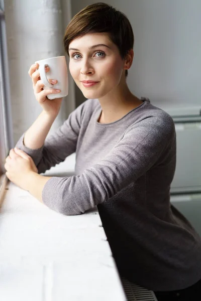 Jovem mulher de cabelos curtos tomando café pela janela — Fotografia de Stock