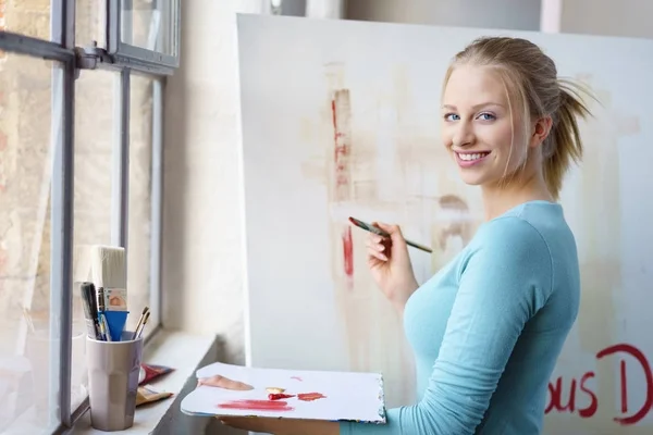 Jonge lachende vrouw schilderij in atelier — Stockfoto