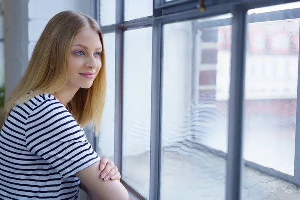 Mladá usmívající se žena při pohledu přes okno — Stock fotografie