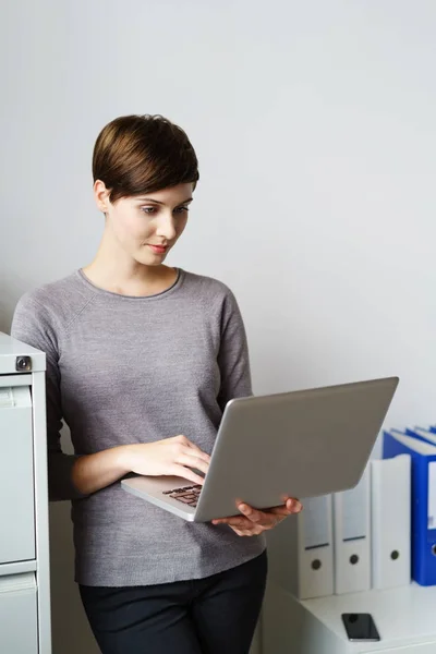 Ung kvinna som står med laptop på kontoret — Stockfoto