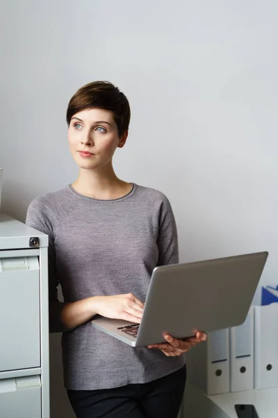 Mujer joven de pie con el ordenador portátil por el gabinete de archivos — Foto de Stock