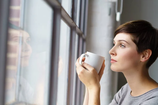 Młoda kobieta zatroskana, picie kawy przez okno — Zdjęcie stockowe