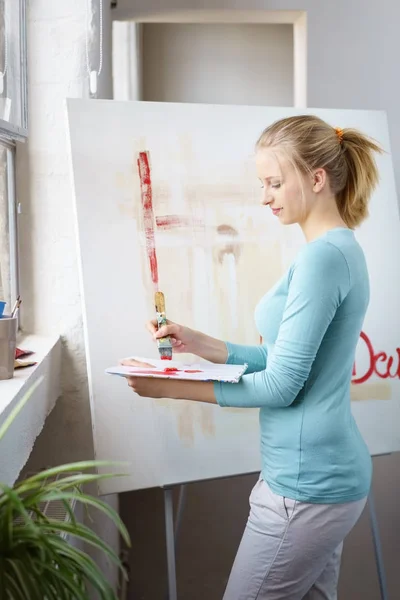 Young blonde woman painting picture in atelier — Stock Photo, Image
