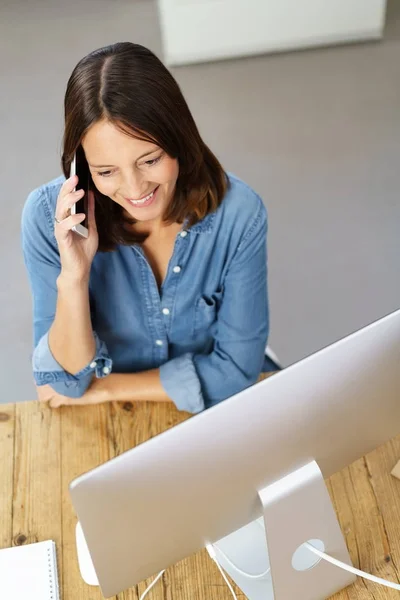 Woman talking on phone in front of computer — Stock Photo, Image