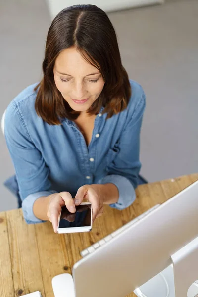 Woman using smartphone phone in front of computer — Stock Photo, Image