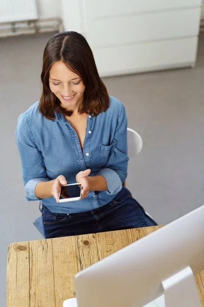 Mujer sonriente usando el teléfono delante de la computadora — Foto de Stock