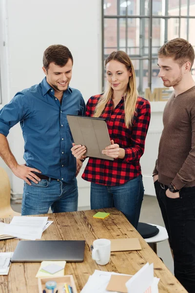 Three motivated young business partners standing looking at tablet pc in office