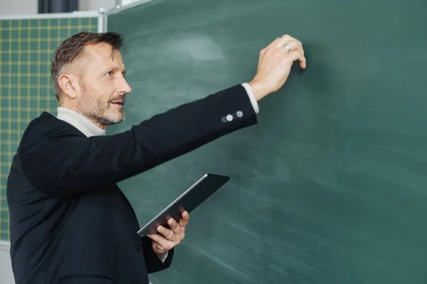 中年男教师手持平板电脑在空白黑板上写字 — 图库照片