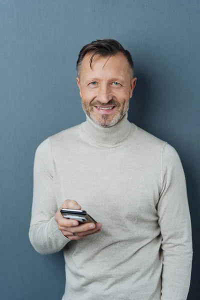 快活な中年男立っている笑顔暗い灰色スタジオ背景手に携帯カメラで — ストック写真